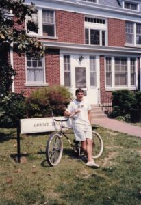 A photo of a man in the late 1980s standing in front of Brent House with his bicycle at Mary Washington College.