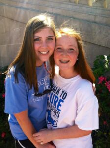 Two sisters, wearing T-shirts supporting finding a cure for type 1 diabetes, hugging and smiling for the camera.