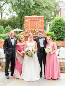 A family of five, including a bride and groom, standing on a patio with an outdoor fireplace.