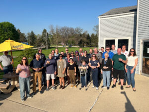 A group of people outside on a patio with a building behind them and a yellow umbrella to their left.