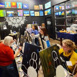 A group of people paint snowmen in a paint bar.