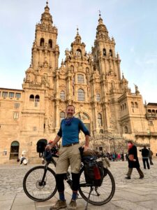 Photo of a man standing in front of a cathedral in Spain with a rented bicycle.