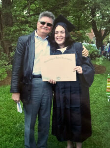 A 2000s photo of a father with his arm around his daughter in her graduation cap and gown holding her diploma.